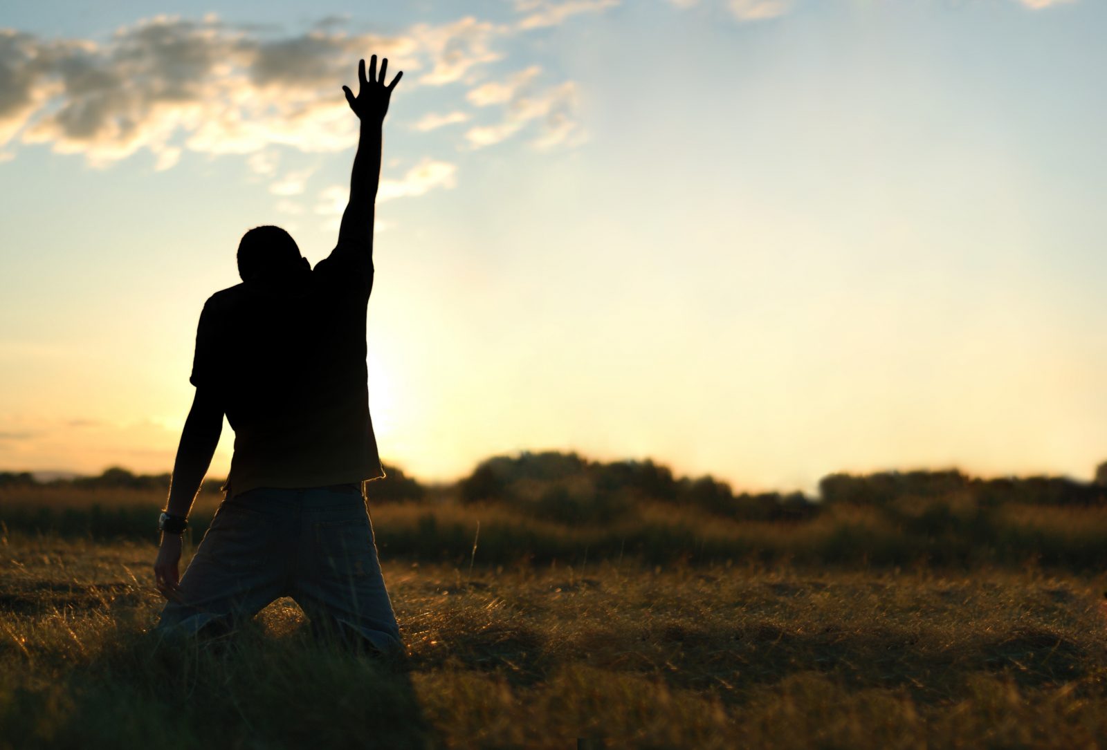 Young man on his knees reaching up to heaven with an outstretched arm.